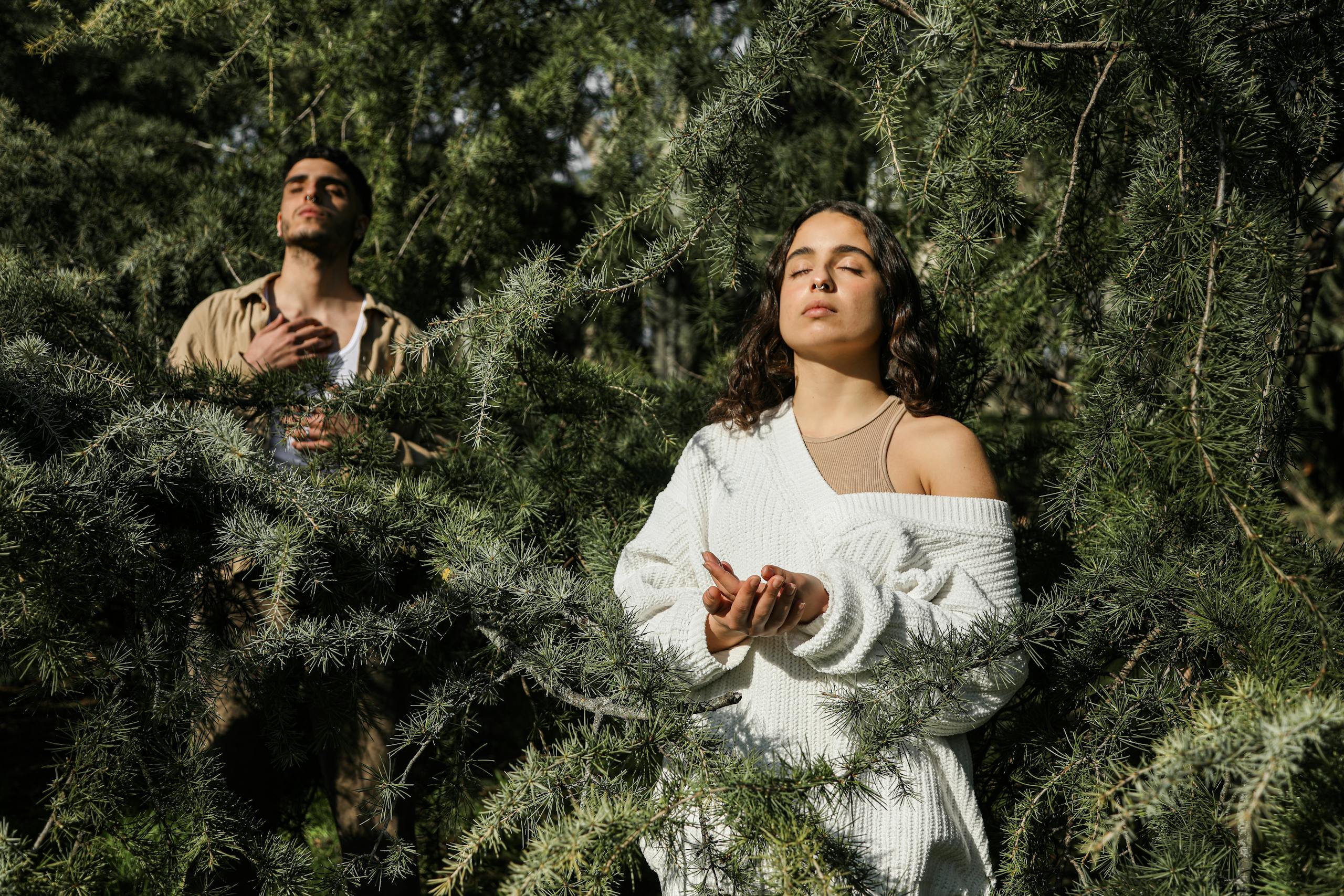 Two adults meditate peacefully amidst lush green trees in a forest.