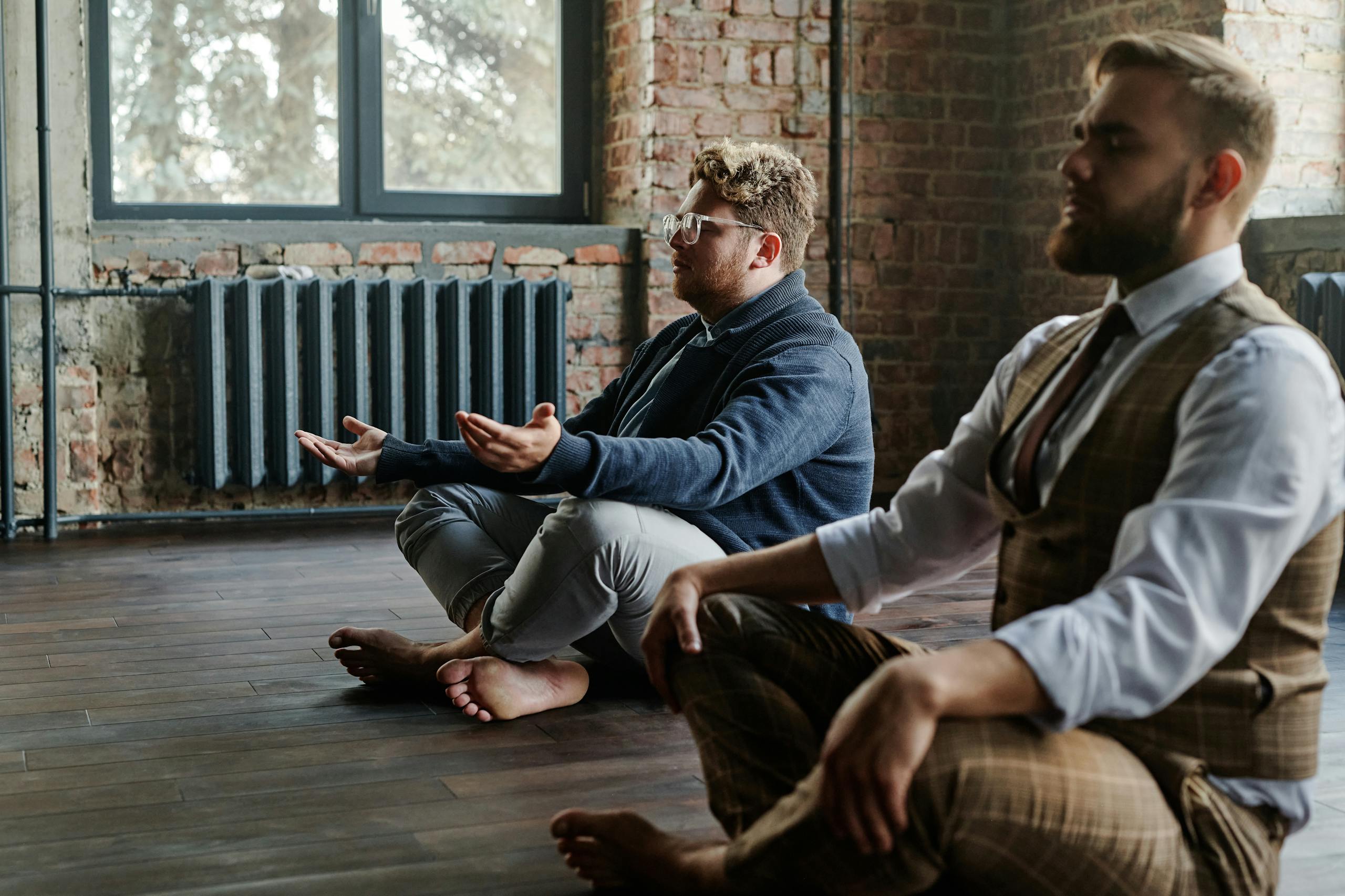 Two men meditating quietly in a rustic indoor setting, promoting mindfulness and relaxation.